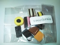A small clear plastic bag labelled "sweetjunkie" contains assorted colourful liquorice allsorts sweets, including yellow, pink, brown, orange, white, and black pieces with various shapes and layered patterns.