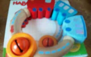 A colourful, circular wooden toy train set with red and blue train engines and two tan curved tracks. The toy features orange knobs with black arrows and is placed on top of a HABA-branded box. The image is slightly blurry.