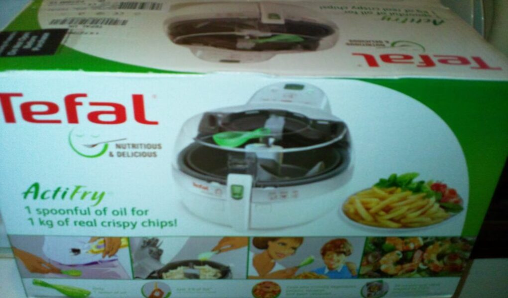 A box of Tefal ActiFry, an air fryer, shows the product image, the Tefal logo, and text stating “1 spoonful of oil for 1 kg of real crispy chips!” Various meal pictures and instructions are visible on the lower part of the packaging.