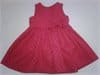 A sleeveless, knee-length red dress for a young girl is laid flat. The dress has a fitted bodice, a flared skirt, and a small decorative bow on the waist’s right side. The fabric appears soft and slightly textured.