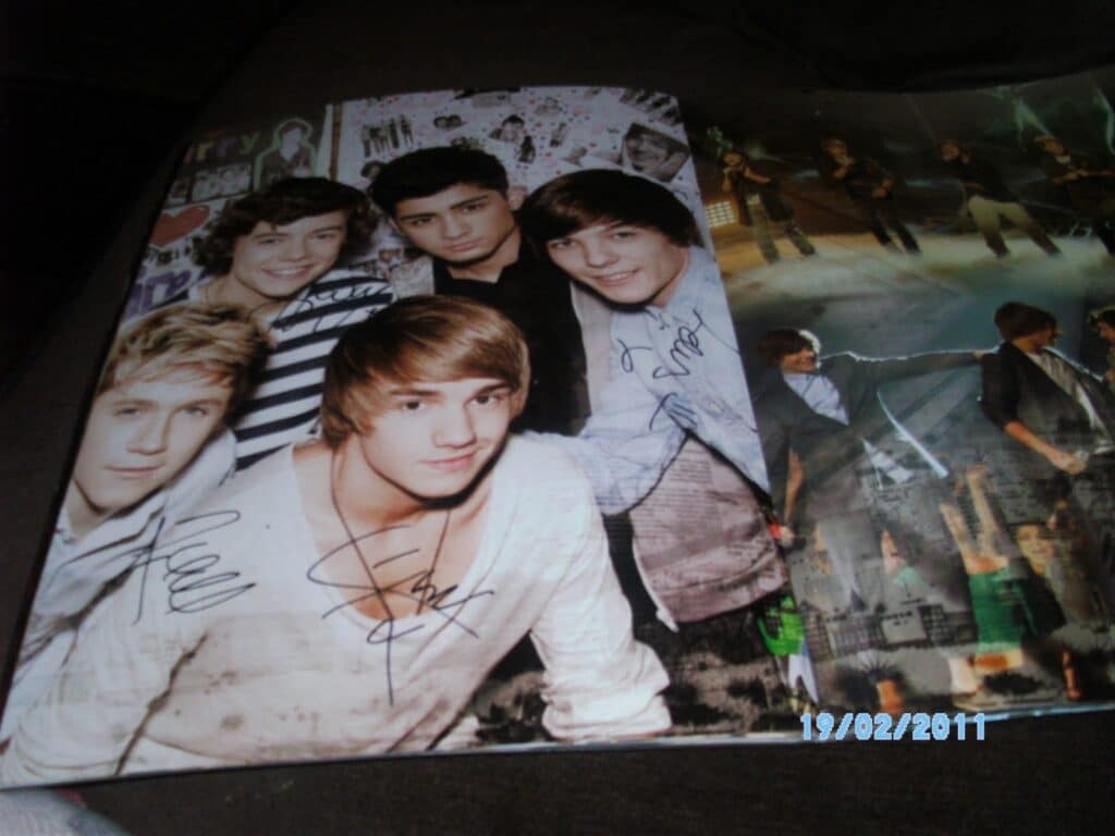 A magazine page shows five smiling young men posing together. Several of their images are autographed with black marker. The opposite page features a group photo on stage. The date "19/02/2011" is stamped at the bottom right.