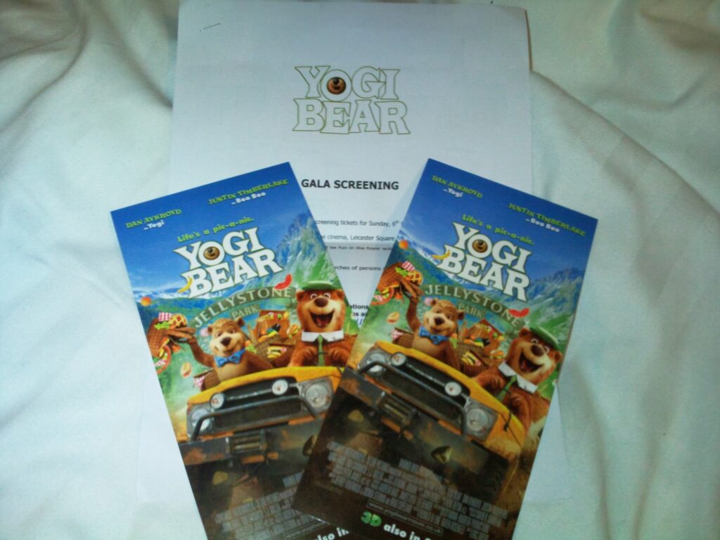 Two colourful “Yogi Bear” cinema tickets sit on a white surface atop a printed sheet labelled “Yogi Bear Gala Screening.” The tickets depict animated characters Yogi, Boo Boo, and Ranger Smith riding in a jeep with a scenic background.