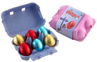 A purple egg box, open to reveal six shiny, foil-wrapped chocolate eggs in gold, red, and blue. Next to it is a closed pink box with a label featuring a red egg and playful graphics.