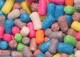 A close-up of colourful cylindrical and pellet-shaped rodent food pieces in shades of blue, pink, orange, yellow, white, purple, and brown. The pieces have a textured surface and are tightly packed together.