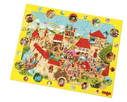 A colourful cartoon puzzle depicts a lively medieval village scene with castles, villagers, and animals. The yellow border features small circular images highlighting individual characters and activities from the main illustration. The puzzle is partially assembled.