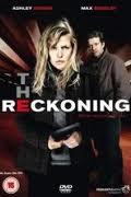 A woman with blonde hair stands in the foreground holding a notepad, looking serious. A man stands behind her in a dark jacket. The title “The Reckoning” appears in bold letters, with "RECK" in red. The background is dark and dramatic.