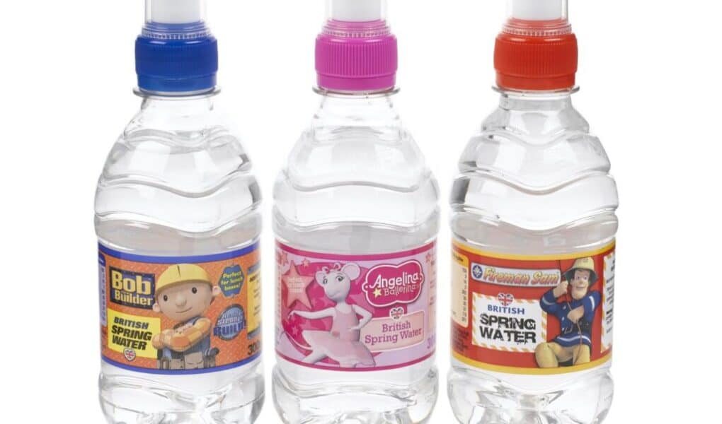 Three clear plastic bottles of water with colourful caps (blue, pink, red) stand side by side. Each features a label with a children’s character: Bob the Builder, Angelino the Pony, and Fireman Sam, with "British Spring Water" text visible.