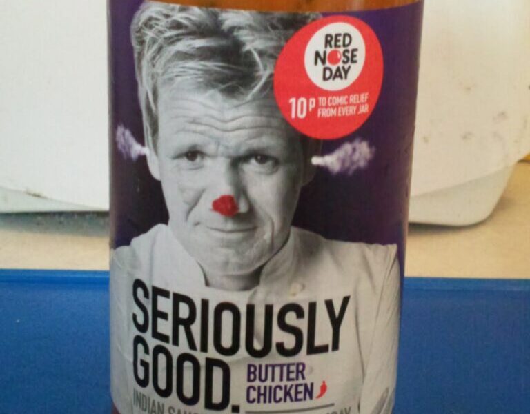 A jar of "Seriously Good Butter Chicken Indian Sauce by Gordon Ramsay." The label shows a black-and-white photo of Gordon Ramsay with a red clown nose. A red circle says, "10p to Comic Relief from every jar" and notes this is for Red Nose Day.
