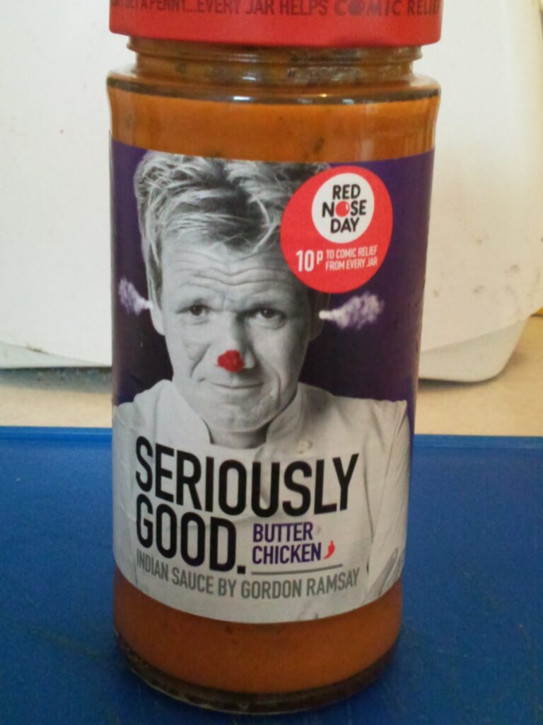 A jar of "Seriously Good Butter Chicken Indian Sauce by Gordon Ramsay" with a black-and-white photo of Ramsay, wearing a red clown nose, on the label. A red sticker on the lid says “Red Nose Day” with “10p to Comic Relief from every jar”.