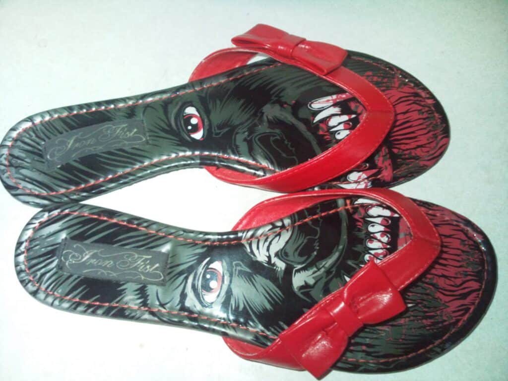 A pair of red sandals with an image of a gorilla face on the insoles; when placed together, the sandals form a complete face with fierce eyes and open mouth showing teeth. The sandals have red straps with bows on top.