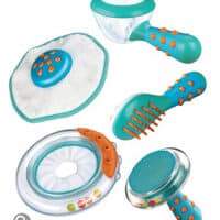 A set of five colourful plastic pet grooming tools in turquoise, white, and orange, including a brush, a round rubber massager, a shedding tool, a round grooming mitt, and a ring-shaped toy with coloured beads inside.