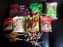 Several colourful bags of assorted sweets are spread out on a dark surface. In front of the bags are various lollipops and individually wrapped sweets scattered loosely, displaying a variety of colours and shapes.