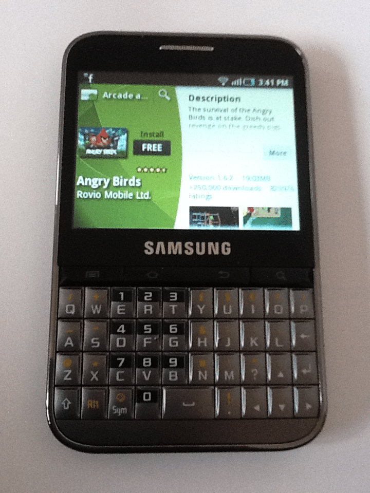A black Samsung smartphone with a physical QWERTY keyboard displays the Angry Birds app page on its screen. The app store interface shows the app icon, install button, description, and stats against a green background. The time reads 15:41.
