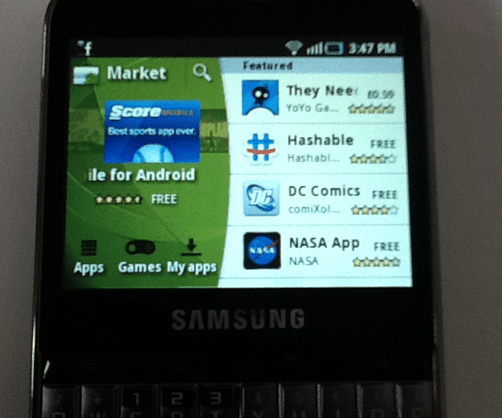 A Samsung mobile phone with a physical QWERTY keyboard displays the Android Market app store. The featured apps include "They Need To Be Fed," "DC Comics," and "NASA App." The time on the phone is 3:47 pm.