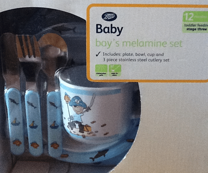 A boxed Boots Baby boy's melamine set, including a plate, bowl, cup, and three stainless steel cutlery pieces with blue handles. The cup features a pirate and sea-themed design. The packaging shows it's suitable for toddlers, stage three, and BPA-free.