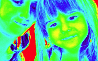 A false-colour thermal-like image shows a woman and a young girl close together, smiling. Their faces appear in blue and green hues, hair in blue and yellow tones, while the background is bright red, creating a vivid, high-contrast effect.