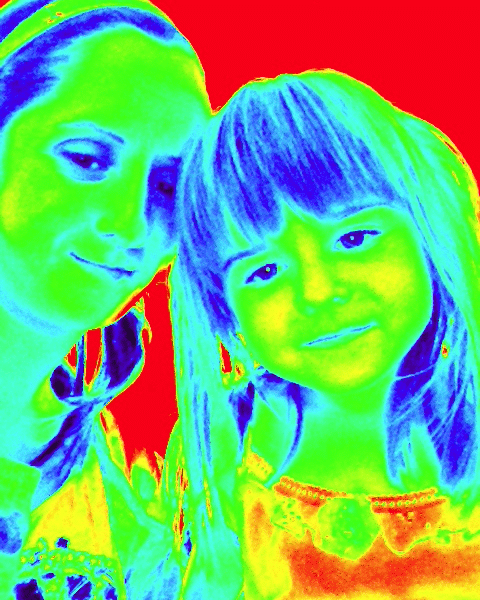 A false-colour thermal-like image shows a woman and a young girl close together, smiling. Their faces appear in blue and green hues, hair in blue and yellow tones, while the background is bright red, creating a vivid, high-contrast effect.