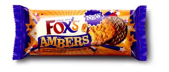 A packet of Fox's Ambers biscuits is shown. The wrapper is purple, orange, and gold with stars and rays. The words "Fox's Ambers" are prominent, along with a "NEW" label, and an image of two golden brown, chocolate-dipped biscuits.
