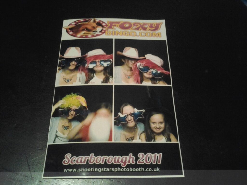 A photo booth printout from "Foxy Bingo" shows two girls wearing playful hats, glasses, and wigs in four different poses. The text reads "Scarborough 2011" with a website for Shooting Stars Photo Booth at the bottom.