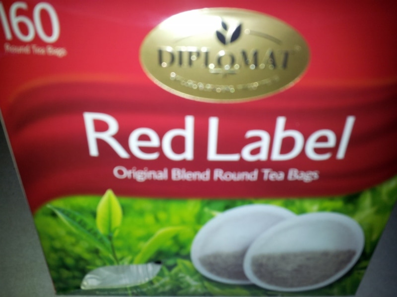 A close-up of a Diplomat Red Label tea box, displaying "160 Round Tea Bags" at the top left, a gold Diplomat logo, and an image of two round tea bags above green tea leaves with a red and white background.