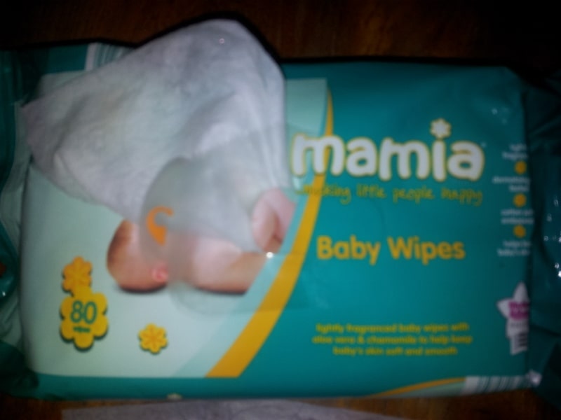 A pack of Mamia Baby Wipes with a partly pulled-out wipe. The packaging is teal with a photo of a baby, yellow accents, and white text. The pack contains 80 wipes and mentions chamomile and aloe for softness.