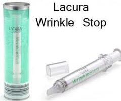 A silver tube labelled "Lacura Wrinkle Stop" is shown, with a clear plastic cap beside it. The product is also pictured upright in its green cylindrical packaging. The words "Lacura Wrinkle Stop" appear in bold black text above.