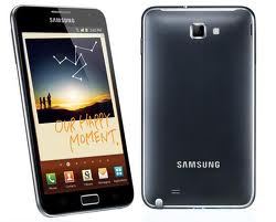 Front and back view of a black Samsung mobile phone. The front shows a touchscreen with an image of three people at sunset and the words "OUR HAPPY MOMENT." The back is plain with a camera and the Samsung logo.