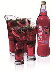 A bottle of Shloer Berry Punch stands beside a clear jug and two glasses, all filled with red berry drink, ice cubes, and mixed berries. The drink has visible slices of fruit and appears chilled and refreshing.