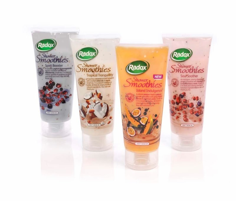 Four Radox Shower Smoothies tubes stand upright on a white background, each with a different fruit-themed design: Spirit Booster (berries), Tropical Tranquillity (coconut), Island Indulgence (passionfruit), and Soul Soother (red berries).