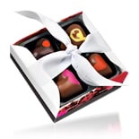 A small box of four assorted chocolates decorated with colourful heart shapes. The chocolates are arranged neatly in a black tray inside a square box, which is tied with a white ribbon bow. The edge of the box has a pink and red design.