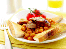 A plate with baked beans, grilled sausages, and roasted tomatoes, served with toasted bread slices. The plate rests on a yellow serviette, with a fork to the left and a glass of orange juice in the background.