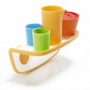 A set of four colourful plastic cups—yellow, orange, blue, and green—placed on a yellow and white tray shaped like a boat. The cups are of different sizes and arranged upright, with the tray balancing on a curved bottom.