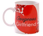 A white ceramic mug with a large red heart design and cluster of small white and red flowers. The mug features the words "Gorgeous Girlfriend" in stylish black and white text across the red heart.
