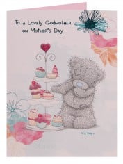 A greeting card with the text “To a Lovely Godmother on Mother’s Day.” It shows a grey teddy bear holding a teacup, standing beside a tiered tray with pink and pastel desserts. The card is decorated with watercolour flowers and a blue butterfly.