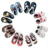 A circle of ten pairs of colourful baby shoes is arranged on a white background. Each pair has different colours and designs, including bows, hearts, and animal faces, creating a playful and cheerful display.