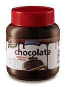 A jar of chocolate hazelnut spread with a red lid. The label shows the spread on a slice of bread, with the word “chocolate” prominently displayed and chocolate drips illustrated along the top edge of the label.