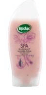 A bottle of Radox Spa Radiant shower cream in a pale pink colour with a white cap. The label features the Radox logo, floral illustrations, and product details. The bottle is sleek and slightly curved, designed for easy gripping.
