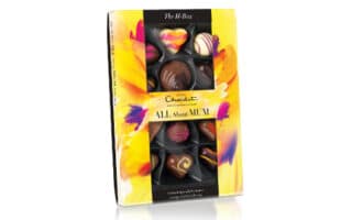 A yellow floral-themed box of Hotel Chocolat chocolates labelled "ALL About MUM" with assorted heart and swirl-shaped chocolates visible through a transparent window on the front. The packaging has a bright, watercolour flower design.