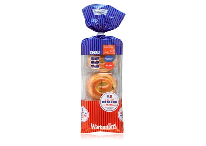 A packaged loaf of Warburtons brioche swirls with visible sultanas, wrapped in a clear bag with blue and red striped design. The label displays "Brioche Swirl" and "Raisin" with French flag colours, and the bread is partially visible through the packaging.