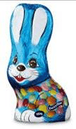 A chocolate bunny wrapped in blue foil with white ears and a painted smiling face. The lower body is decorated with colourful spots, resembling Easter eggs. The bunny has wide eyes, a red nose, and a cheerful expression.