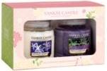 A gift box contains two Yankee Candle jars—one white and one purple. The box has a floral design, a clear window showing the candles, and the label “Yankee Candle” at the top. The candle labels display different scents.
