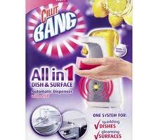 A Cillit Bang All in 1 Dish & Surface automatic dispenser is shown with a hand holding a red sponge under the nozzle. The background is purple with lemons at the top, and text highlights its use for sparkling dishes and gleaming surfaces.