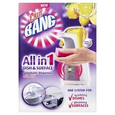 A Cillit Bang All in 1 Dish & Surface automatic dispenser is shown with a hand holding a red sponge under the nozzle. The background is purple with lemons at the top, and text highlights its use for sparkling dishes and gleaming surfaces.