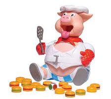 A plastic pig chef toy with a white chef's hat, red scarf, and white apron sits with a spatula in one trotter. Its mouth is open wide and it appears excited. Colourful plastic burger pieces are scattered in front of it.