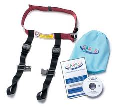 A child aeroplane safety harness with black straps and a red belt is displayed next to a light blue drawstring bag labelled "CARES." Also shown are an instruction manual and a DVD, both branded with the CARES logo.