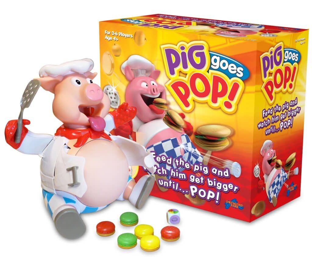A toy game called "Pig Goes Pop!" featuring a plastic pig chef holding a spatula, with a bulging belly and colourful plastic burger pieces. The pig sits beside the game box, which shows the pig and burgers with the game's logo and instructions.