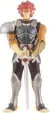 A toy action figure of a male warrior in black and silver armour with a single shoulder pad, red hair, and yellow skin, holding a silver sword vertically with both hands. The figure stands upright against a plain white background.