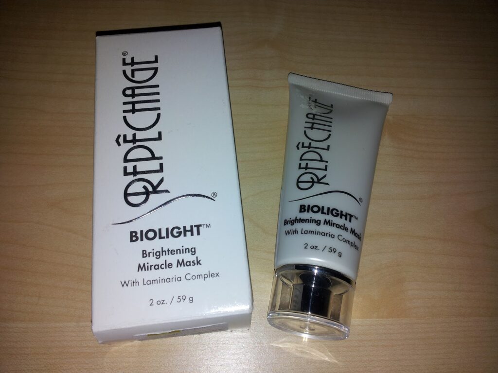 A white box and matching tube of Repêchage BIOLIGHT Brightening Miracle Mask with Laminaria Complex, 2 oz / 59 g, are shown on a light wooden surface. The items are positioned side by side, with the box on the left and the tube on the right.