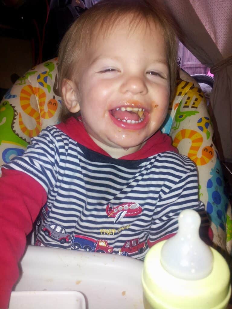 A child sitting in a highchair with food on it.