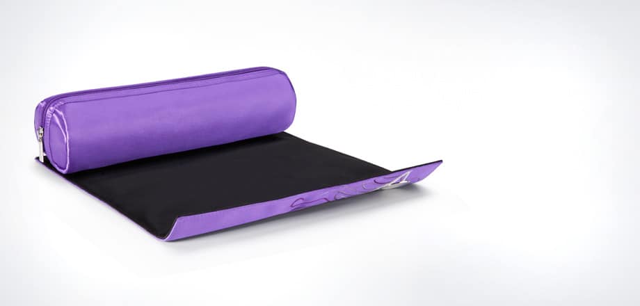 A purple rectangular pencil case with a zip-fastened top is attached to a flat, matching purple mat. The mat is partially unrolled, revealing a black interior with a corner folded, exposing a decorative design. The background is white and minimalistic.
